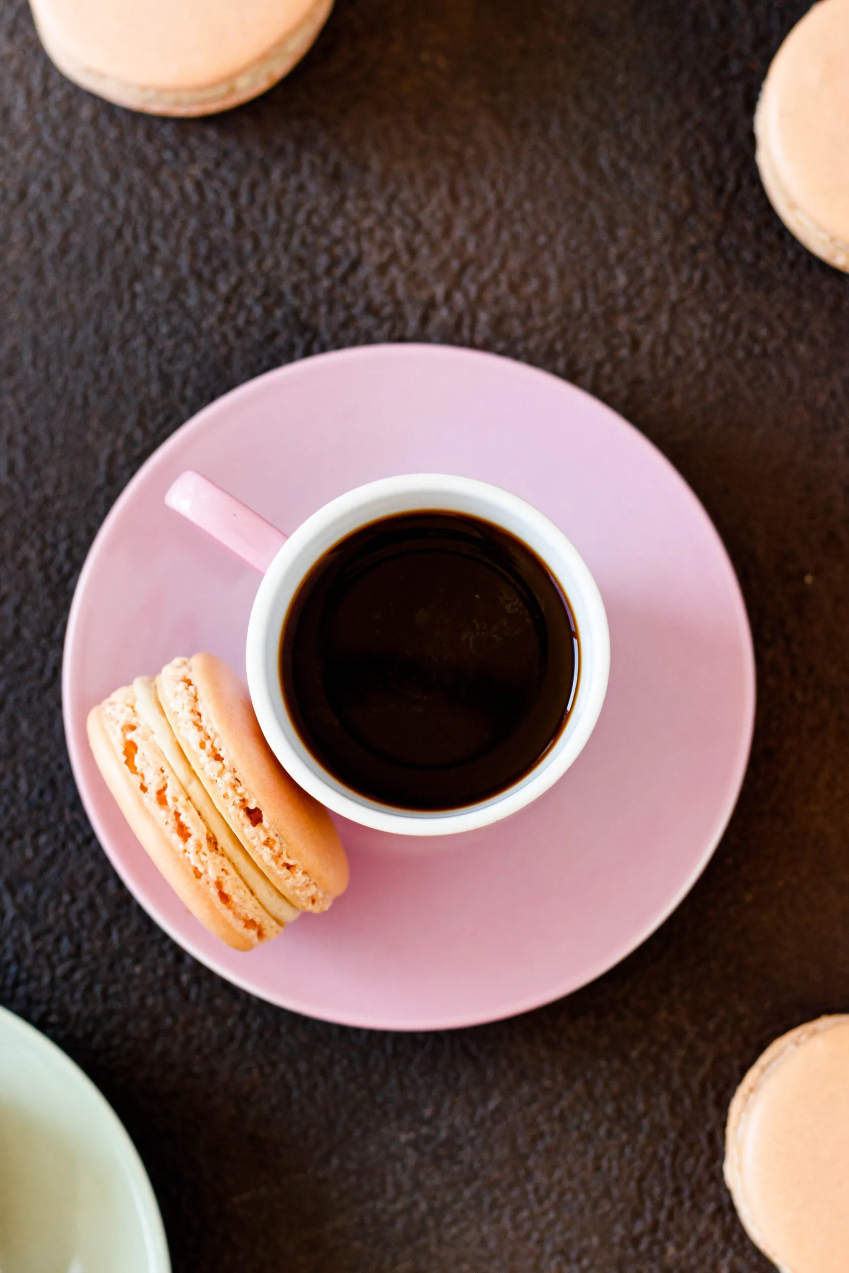 top view of a shot of Cuban coffee in a pink espresso mug sitting on a pink saucer with a cuban coffee macaron balanced alongside 