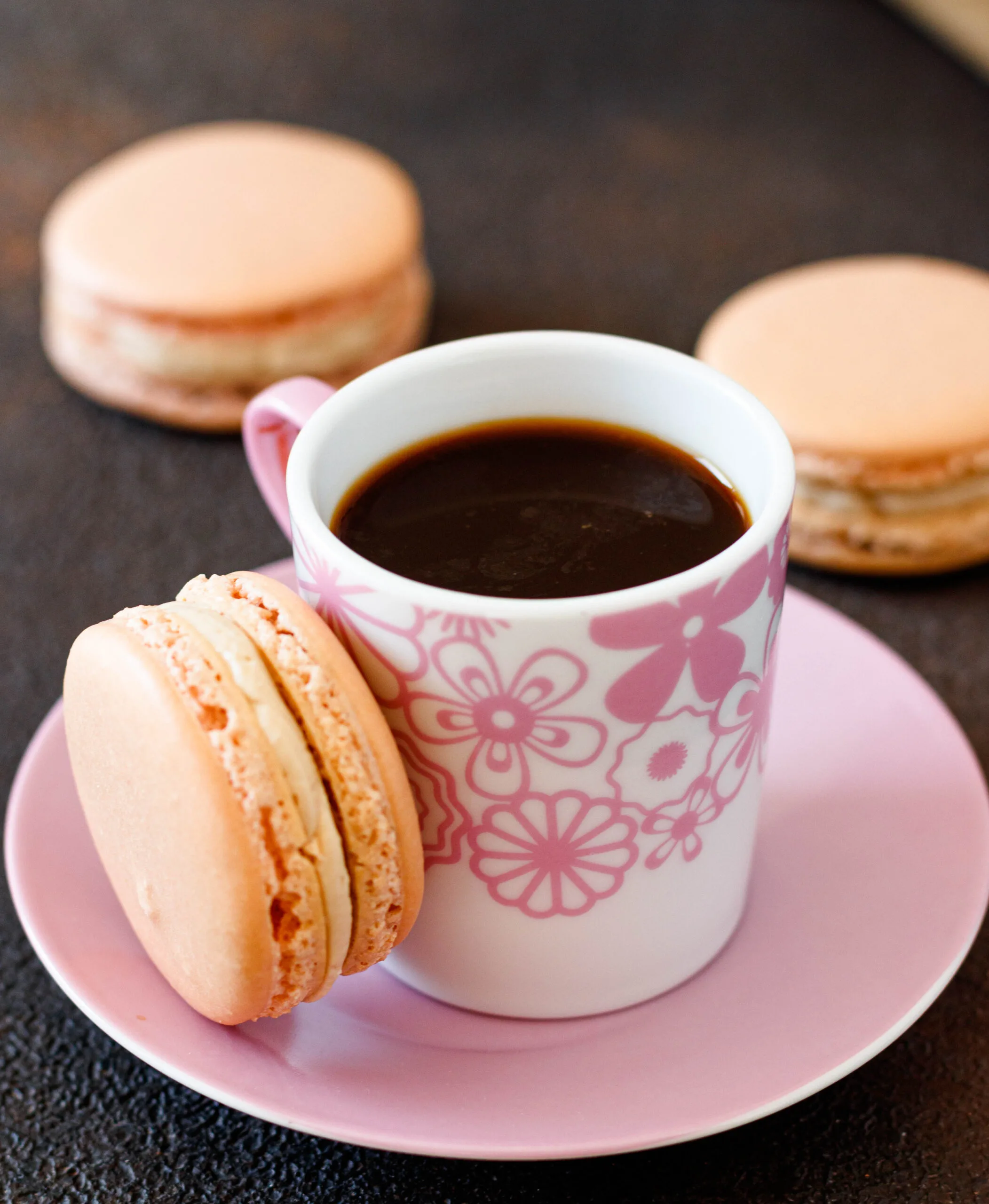 close up angled picture of the macaron alongside the shot of espresso in a pink floral cup on a pink saucer