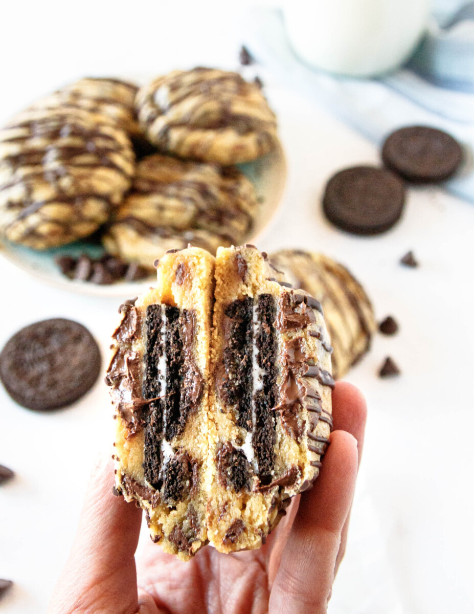 close up of a hand holding an oreo stuffed chocolate chip cookie cut in half. 
