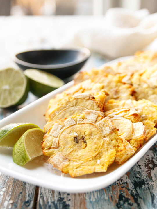 plated air fryer tostones on a rectangular white plate with lime wedges ready to enjoy
