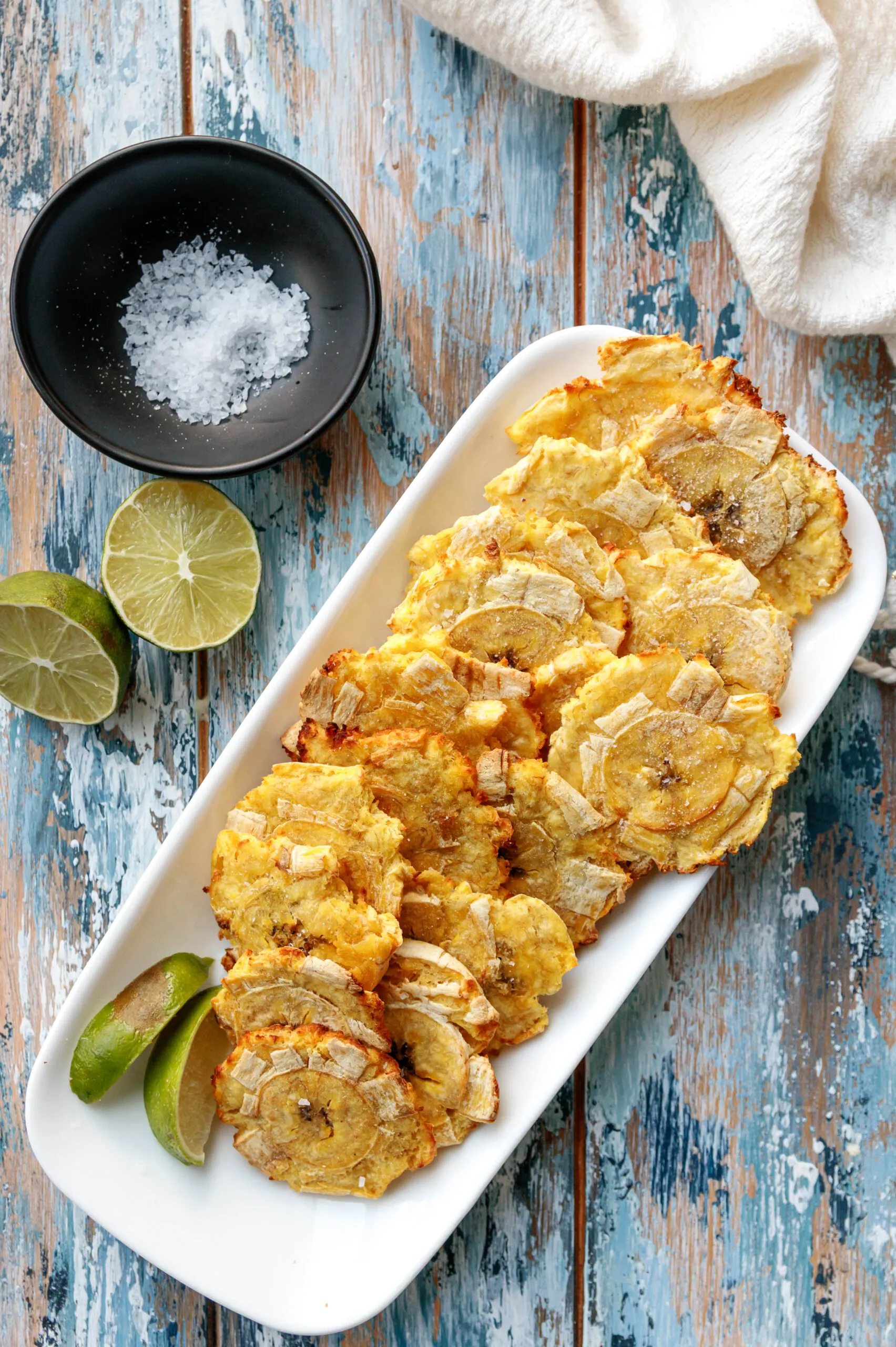 top view of the tostones on a mottled blue background with a dish of salt and cut lime as garnishes
