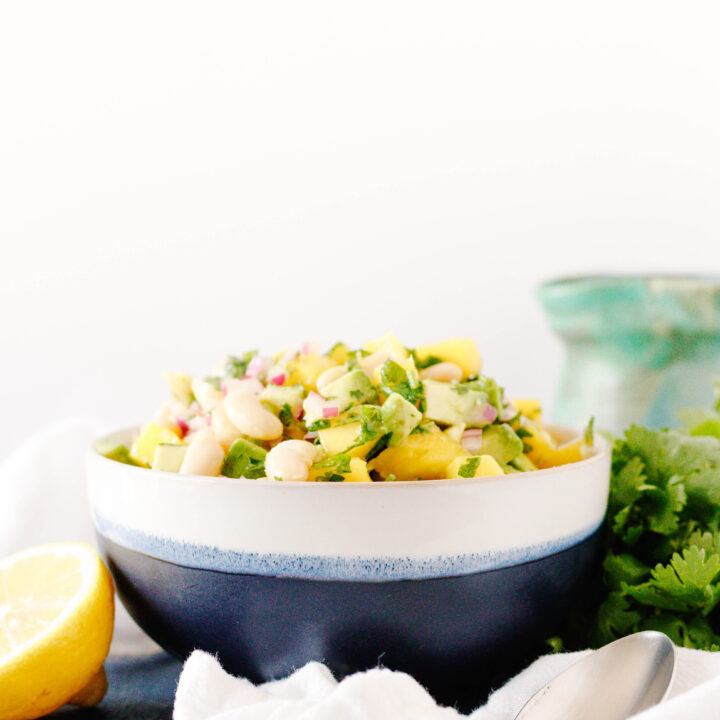 easy mango avocado salad in a white and blue bowl sitting on a blue tabletop with a white background.