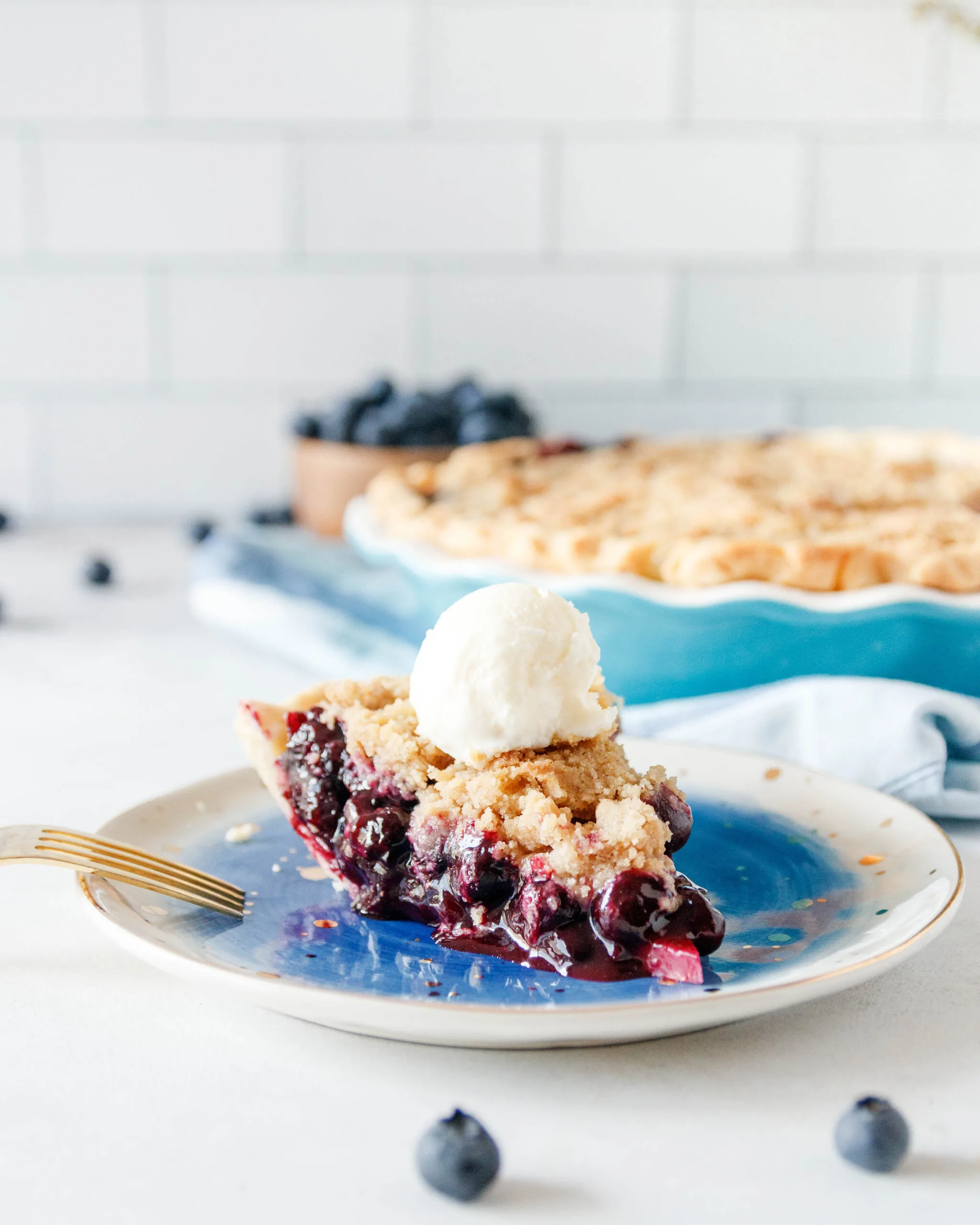 slice of blueberry pie on a plate with a scoop of vanilla ice cream on top
