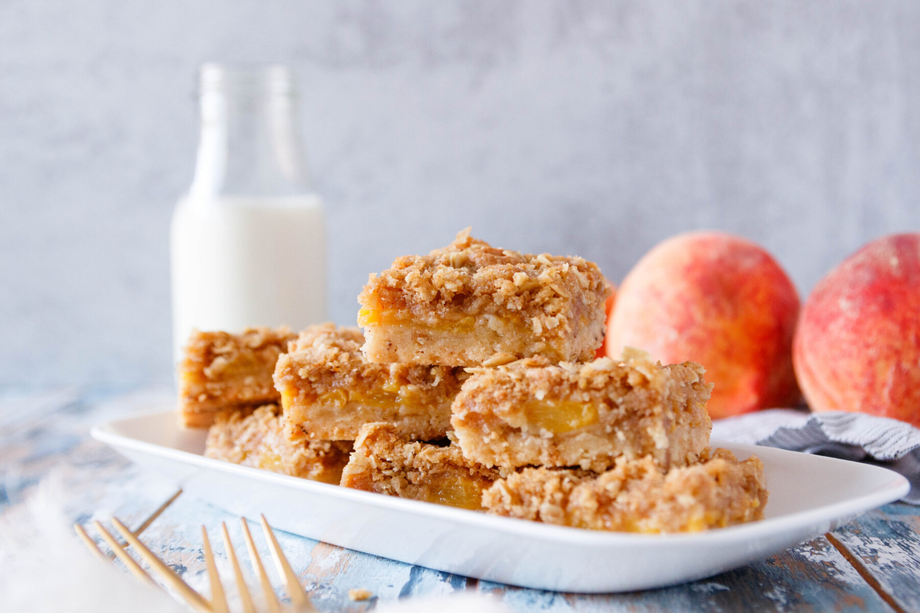 horizontal image of the peach bars on a white rectangular platter with a jug of milk and fresh peach in the background
