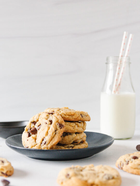stacked chai chocolate chip cookies on a black plate with a bottle of milk with two straws in the background