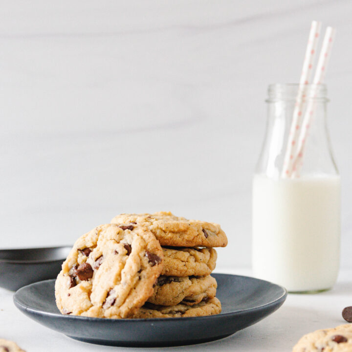 stacked chai chocolate chip cookies on a black plate with a bottle of milk with two straws in the background