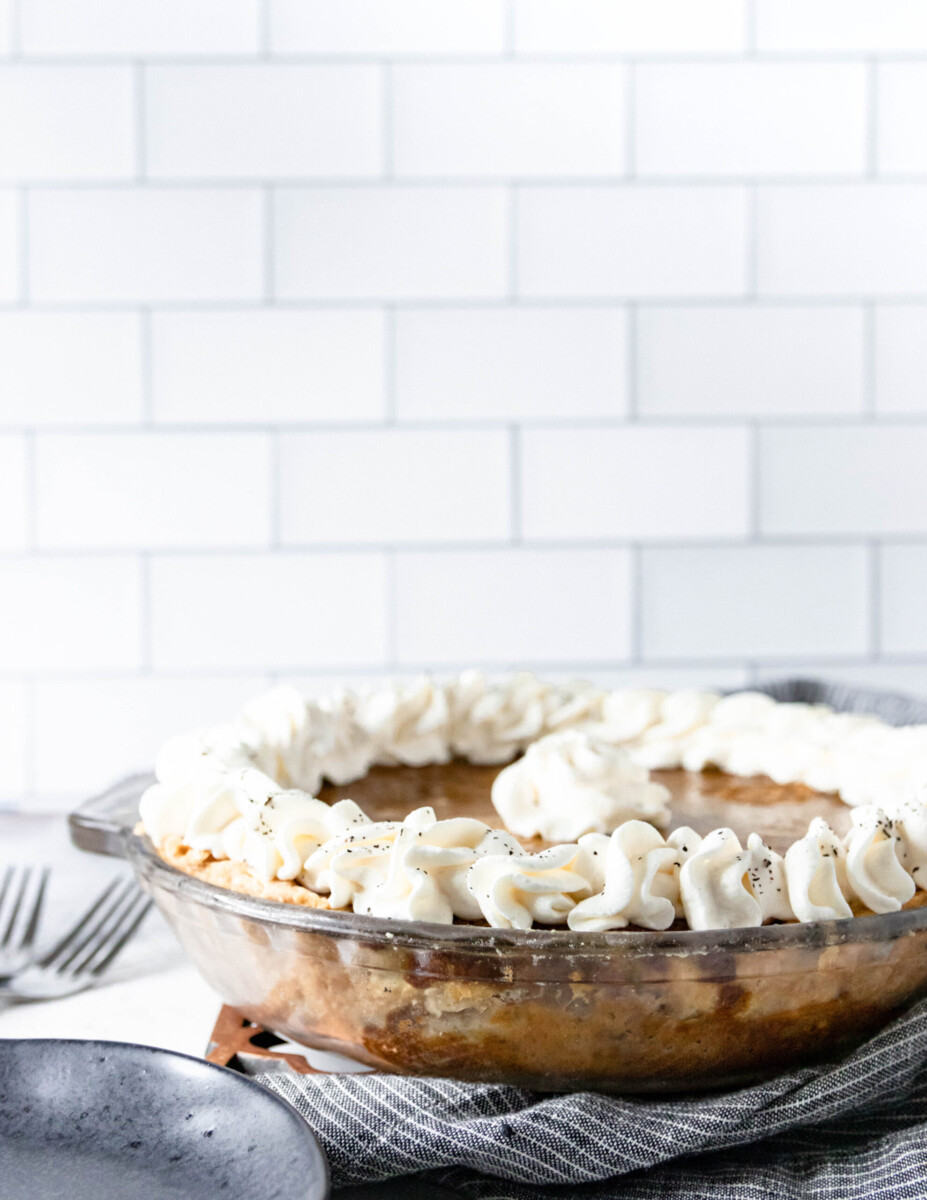 pumpkin chai pie with whipped cream decorations in a glass plate on a light counter with white subway tile background