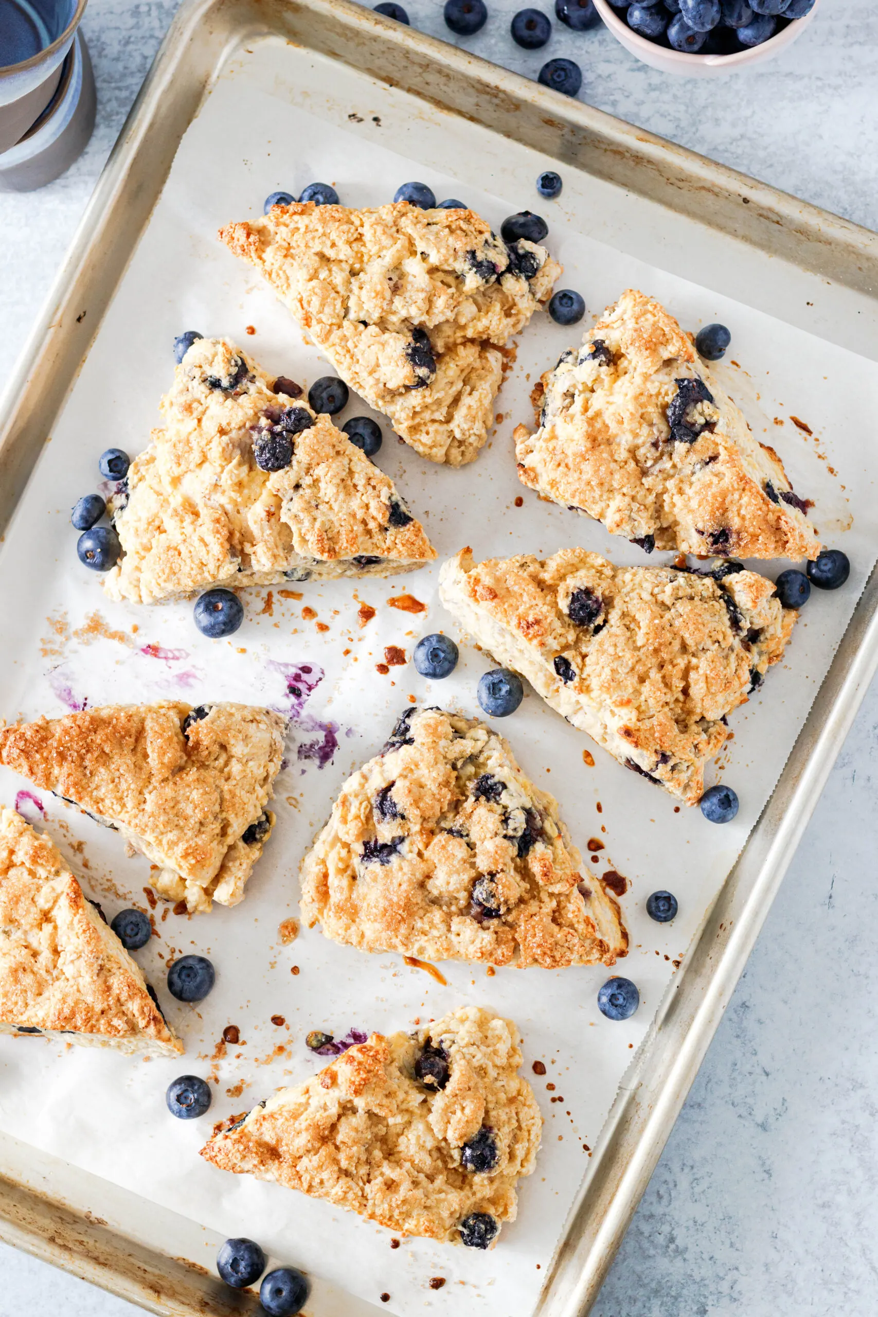 Top view of the baked scones on a light aluminum rimmed baking sheet with scattered blueberries