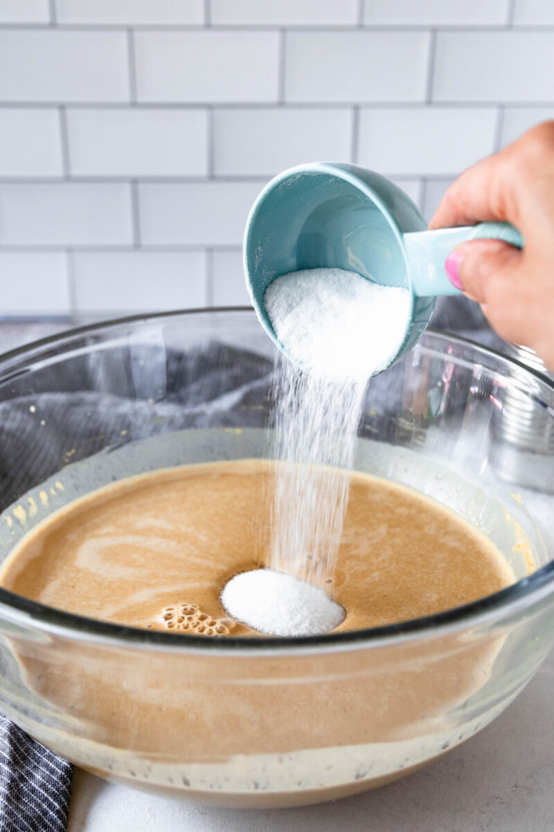 sugar being poured into a glass mixing bowl