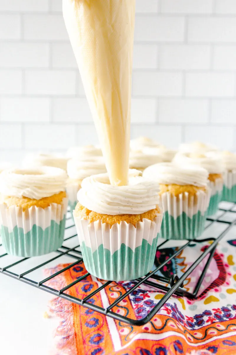 using a piping bag to pipe the pastry cream into the frosted cupcakes.