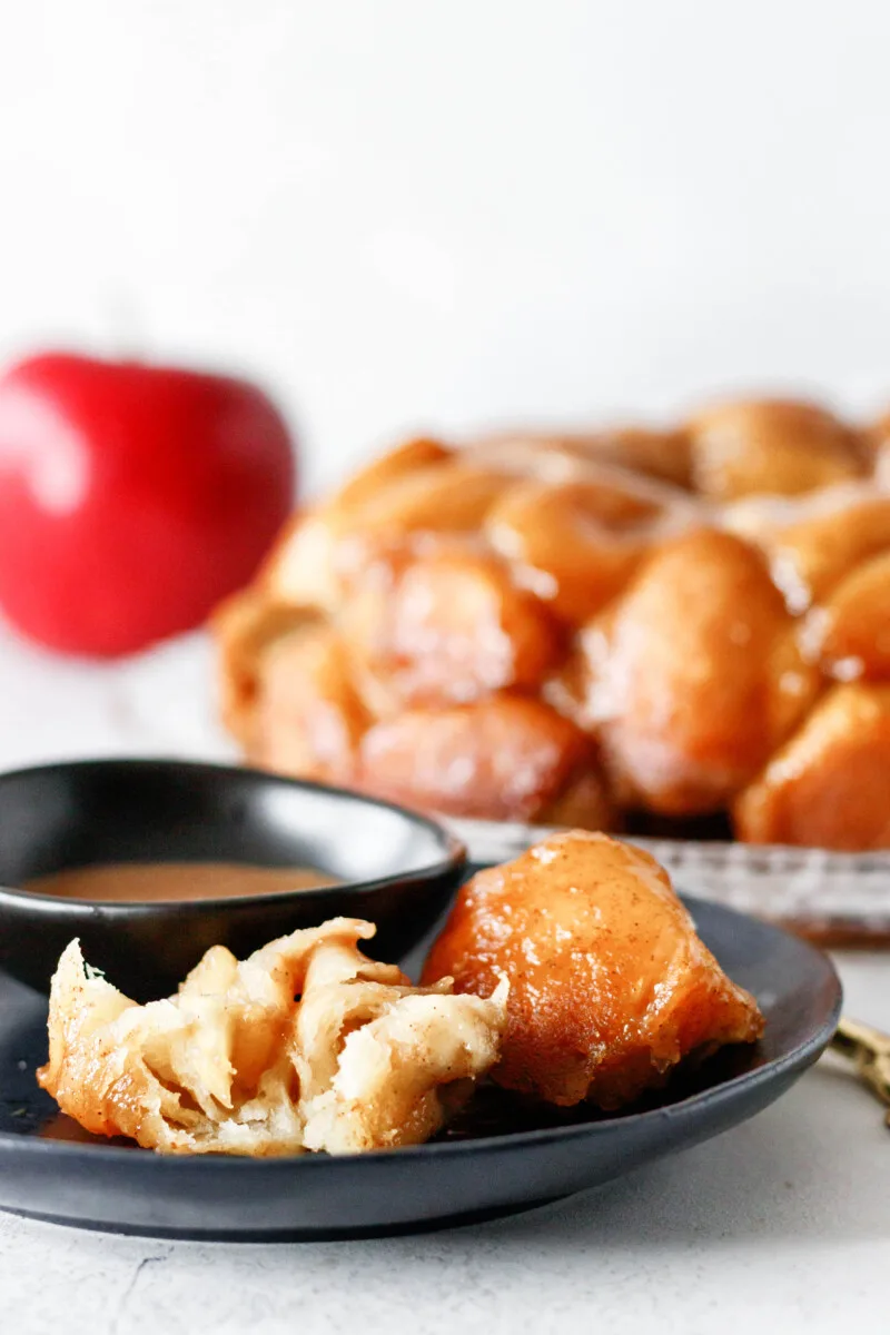 a bite of caramel apple monkey bread cut open on a black plate to show the apple pie filling