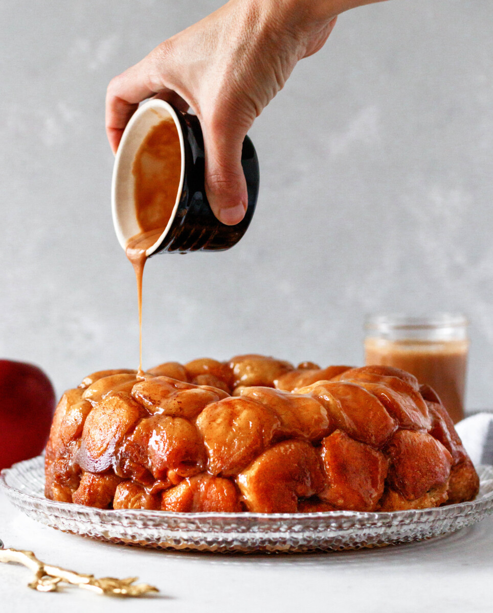 hand pouring caramel glaze over the baked monkey bread