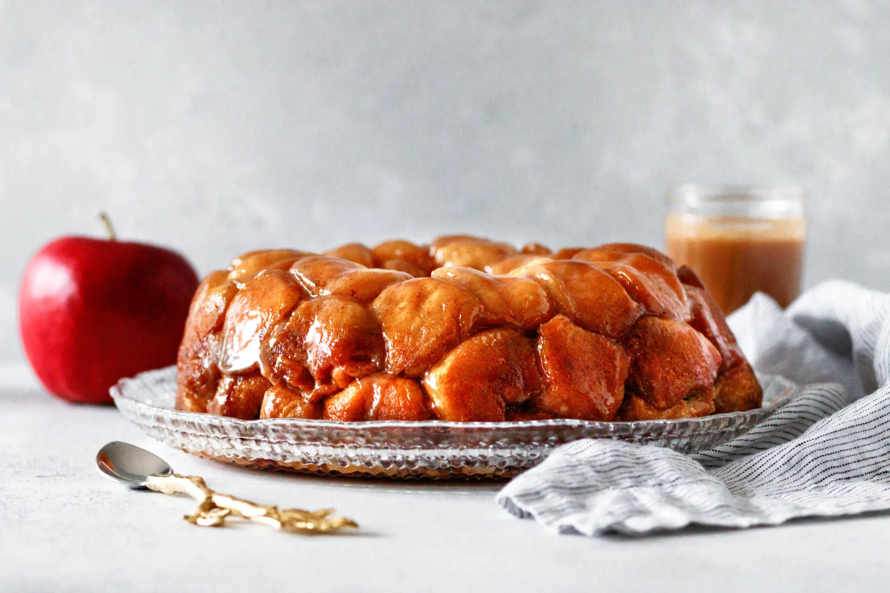 horizontal image of the baked monkey bread, gleaming on a cut glass plate set on a light photography drop with mottled grey background