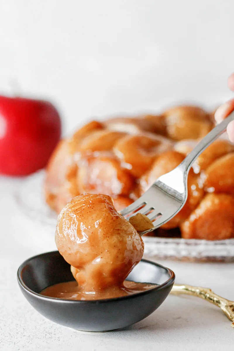 bit of apple monkey bread on a fork dipping into caramel sauce
