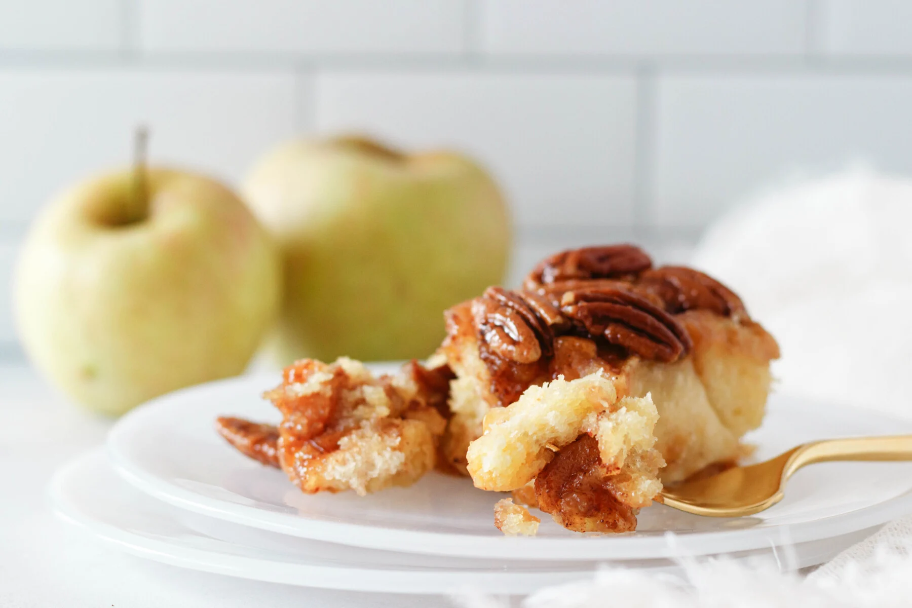 horizontal image of an apple sticky bun on a plate. There's a portion torn out of the bun for a closer look at the final texture and baked filling