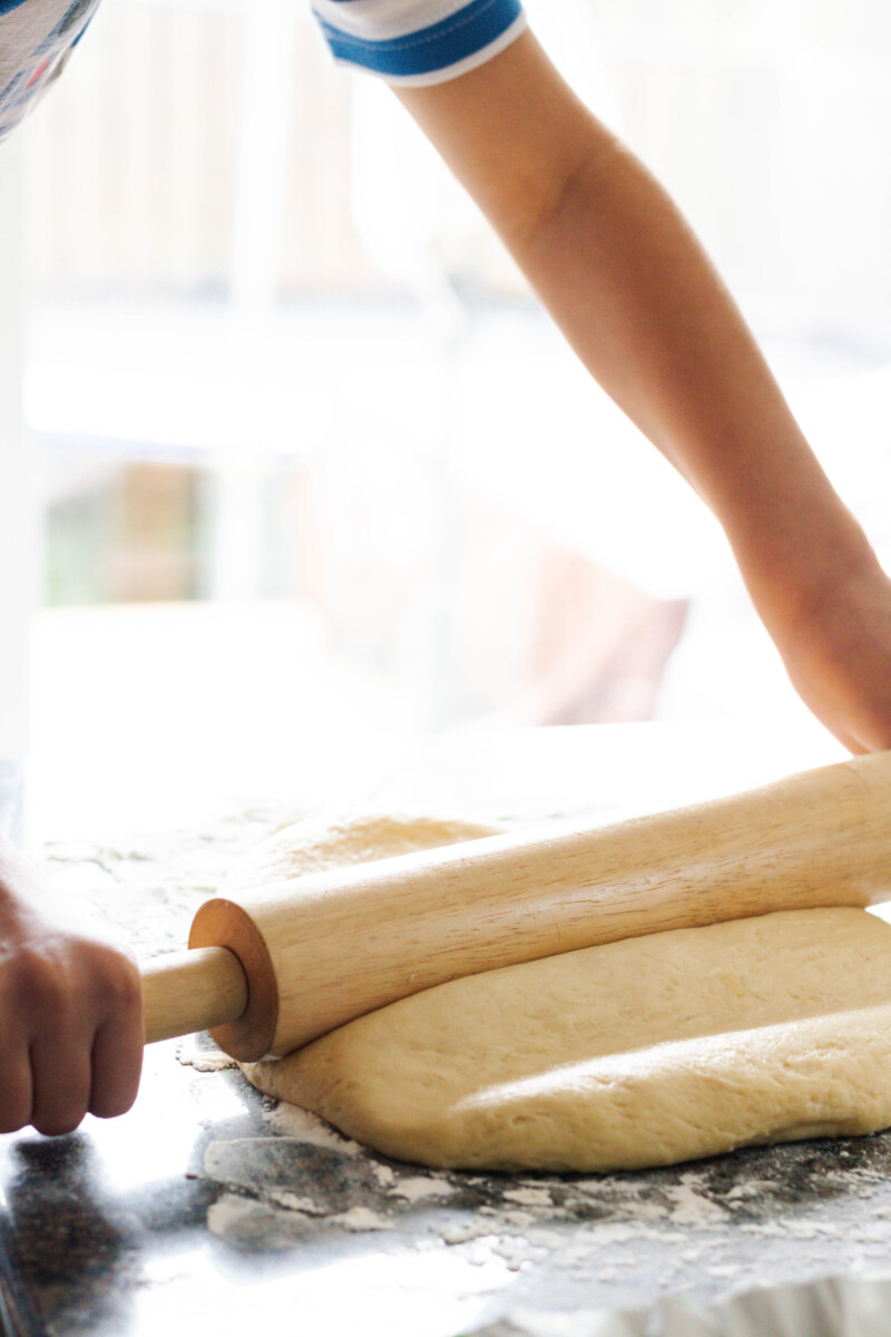 hands rolling out sticky bun dough with a wooden handled rolling pin