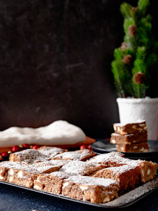 gingerbread brownies cut and dusted with powdered sugar on a black plate