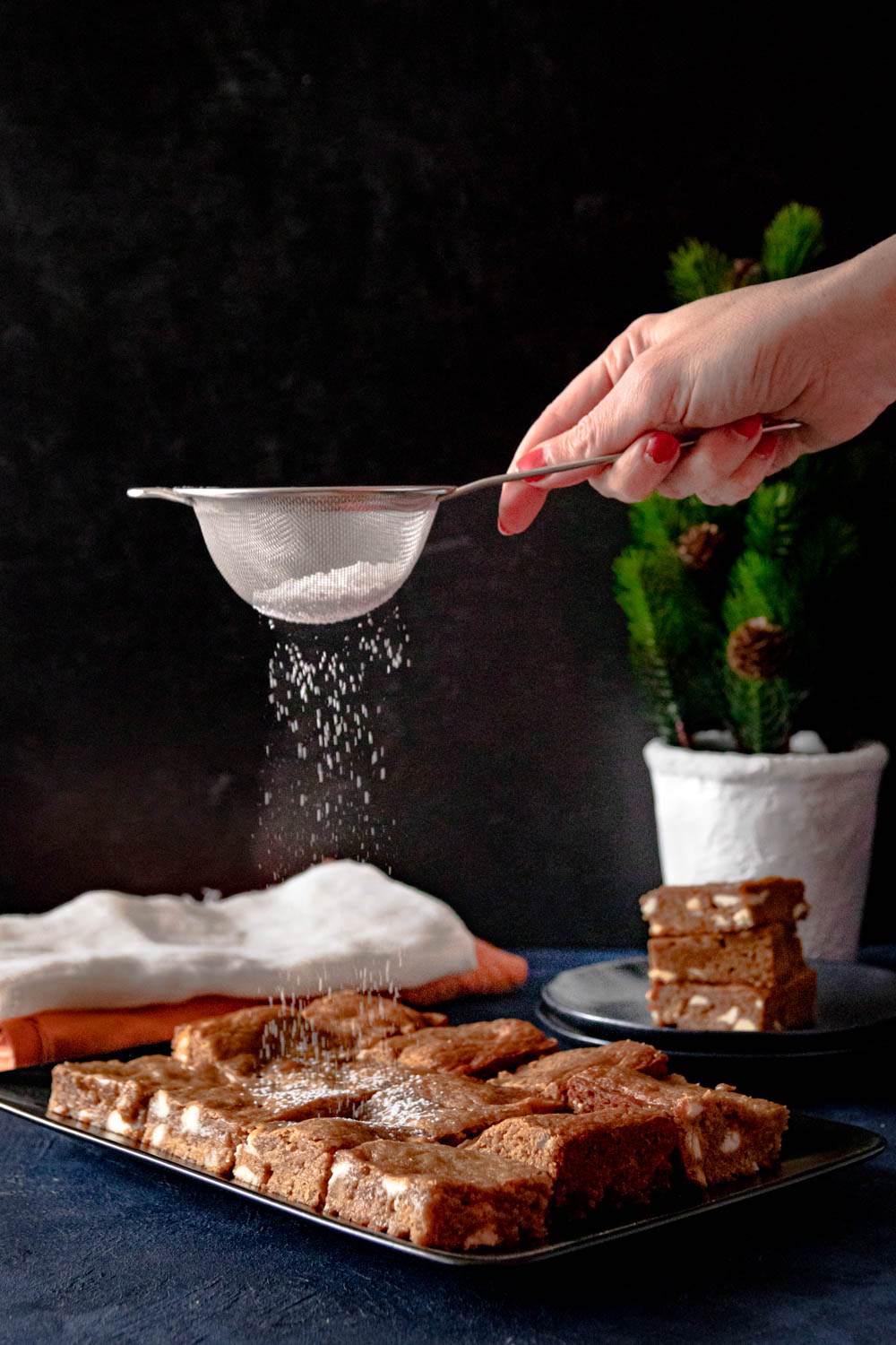 A hand using a small sieve to dust the brownies with powdered sugar.