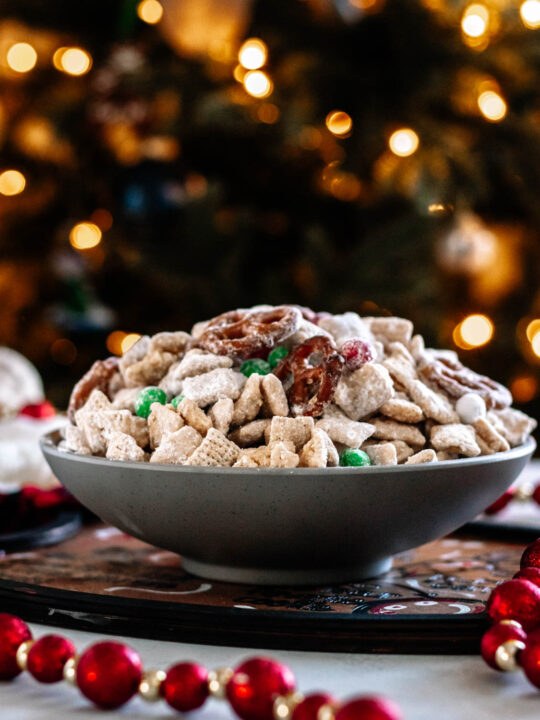 Give Santa what he wants! A bowl of Christmas Muddy Buddy Mix in a grey bowl set in front of a lit Christmas tree