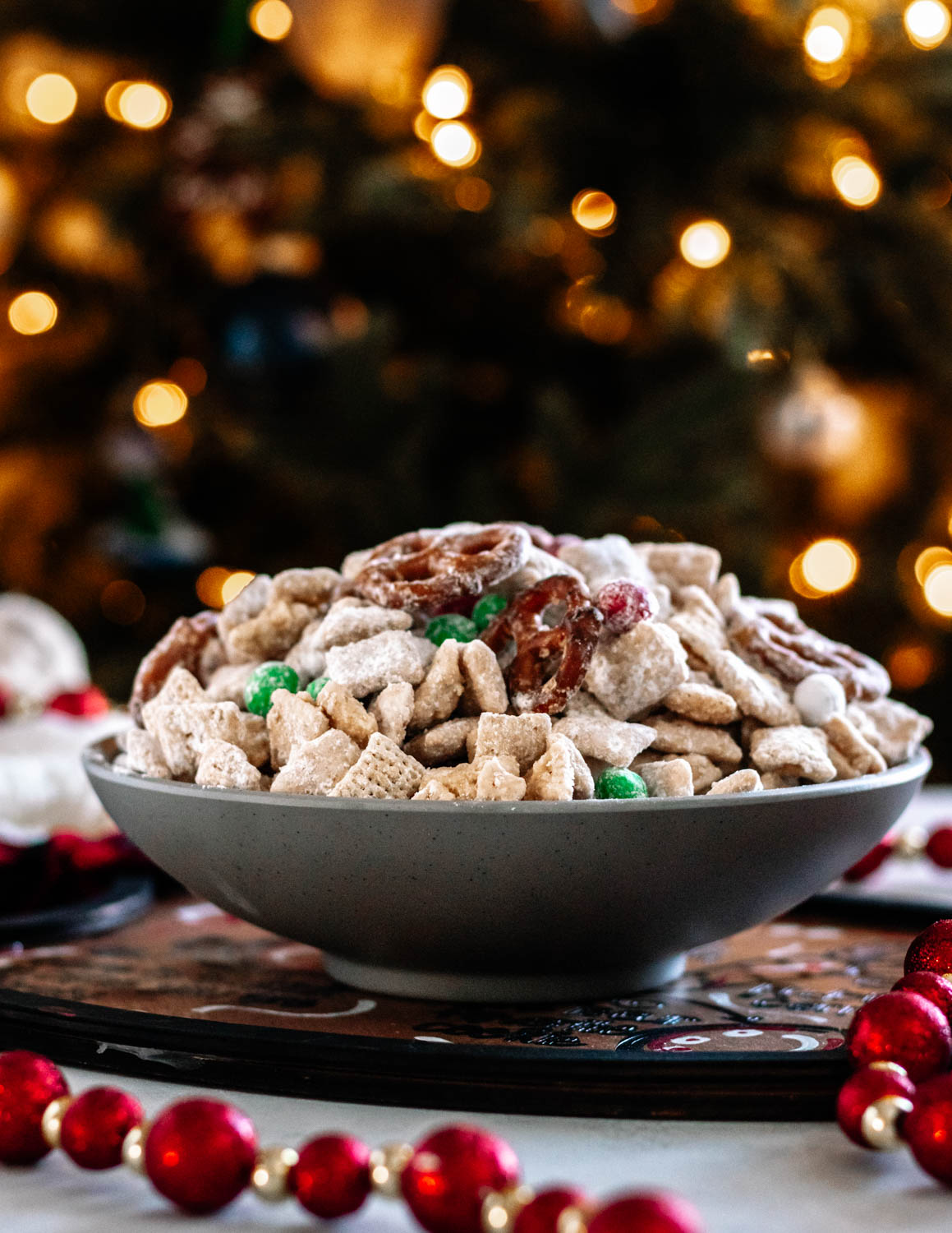 Give Santa what he wants! A bowl of Christmas Muddy Buddy Mix in a grey bowl set in front of a lit Christmas tree