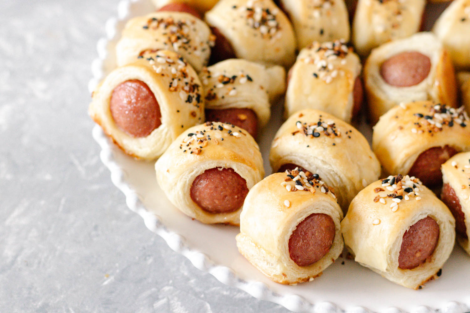 horizontal image of the prepared puff pastry hot dog bites on a plate. Taken at about a 45 degree angle and a little closer to show texture.