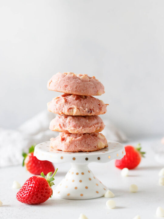 Four strawberry cookies stacked on a white cupcake stand with gold polka dots