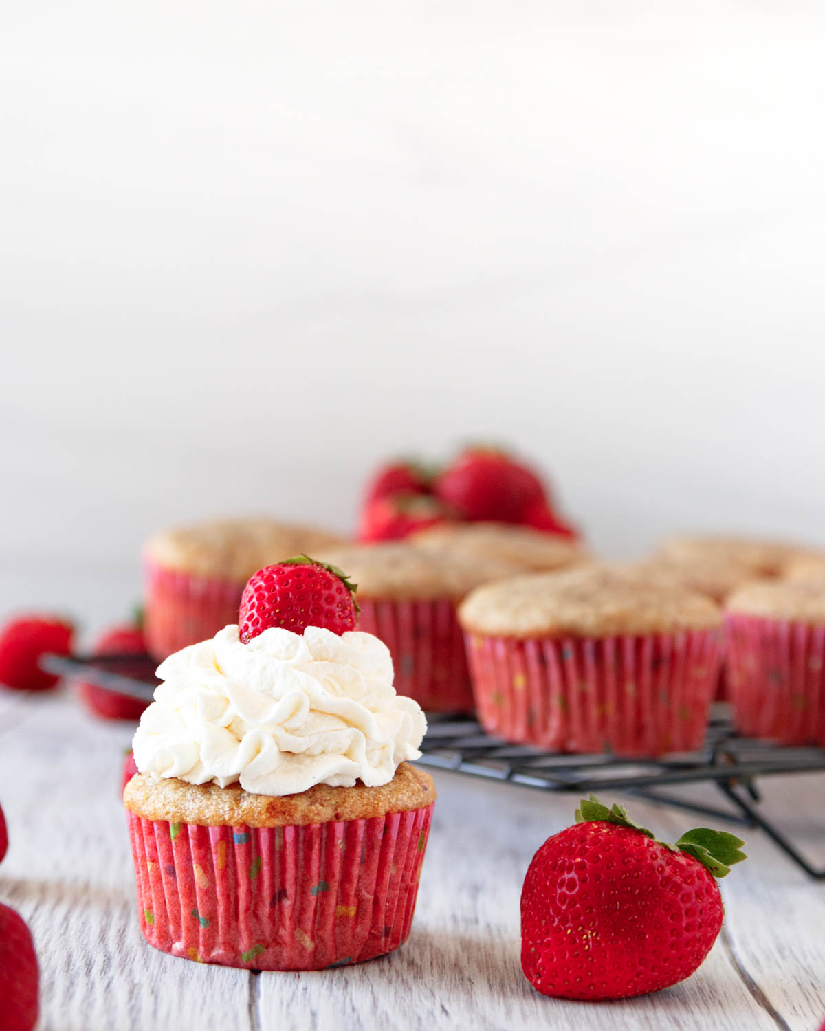 There is a decorated cupcake in the foreground of the image, but in the background you see a cooling rack full of undecorated cupcakes with a pink-ish hue - this is the natural color, not a bright pink.