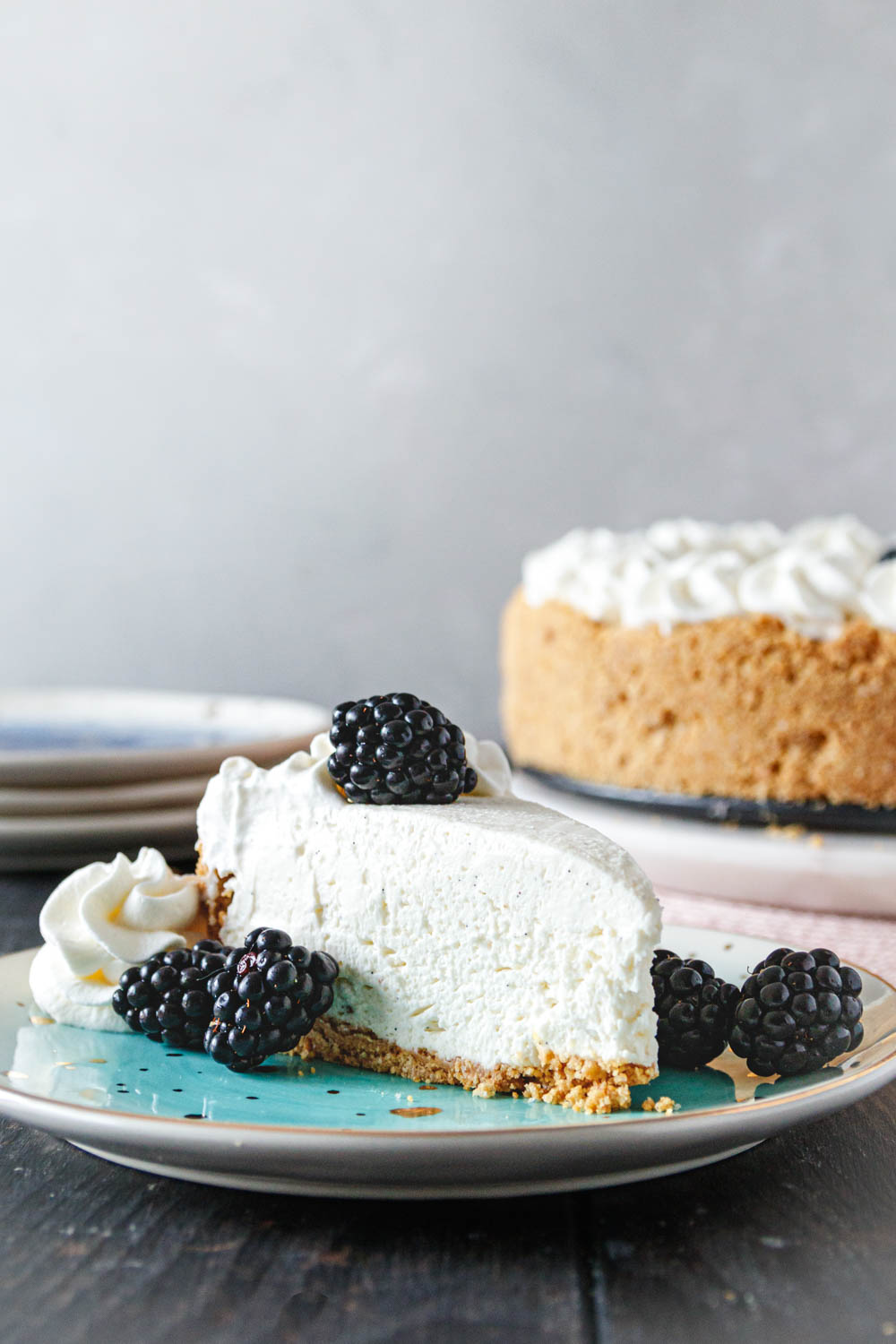 slice of cheesecake on a plate with blackberries and a bit of stabilized whipped cream