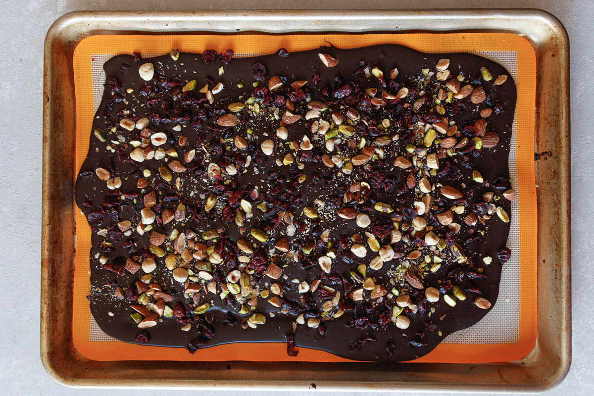 Chocolate bark on a baking sheet lined with silicone, after spreading the melted chocolate and adding the toppings