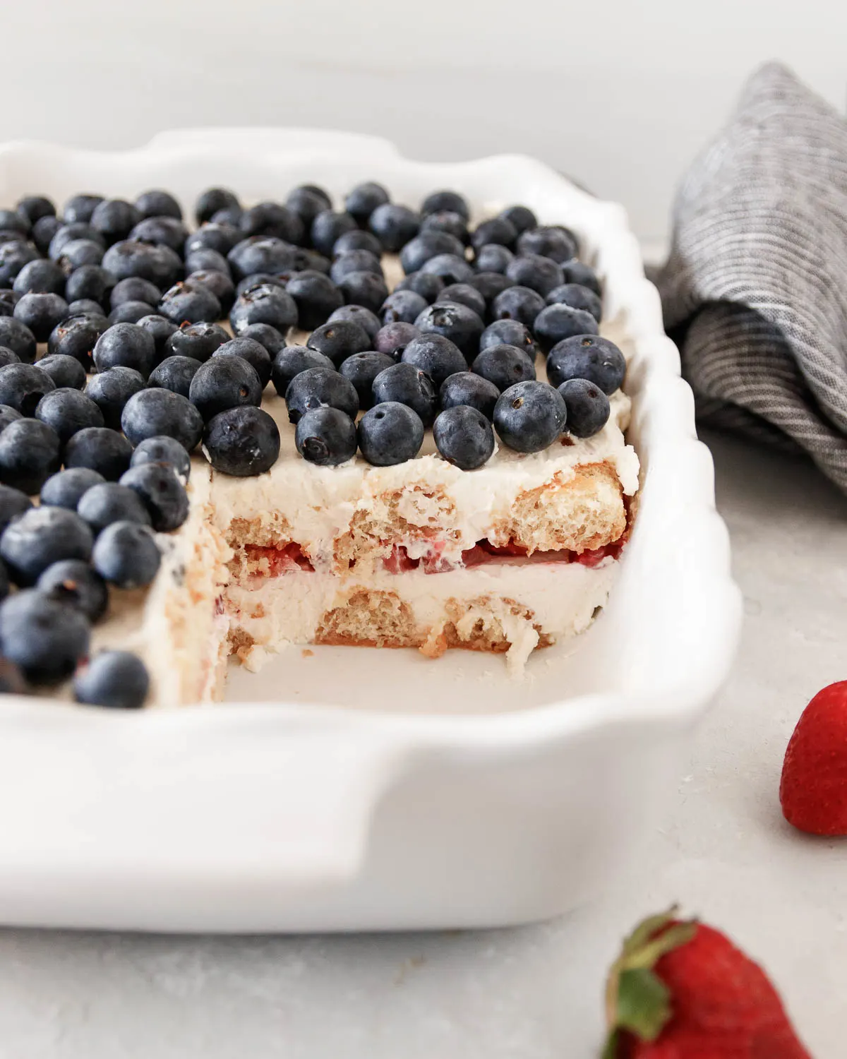 Close up of the strawberry tiramisu in the casserole dish after a slice has been removed. This shows a cross-section of the red, white, and blue layers.