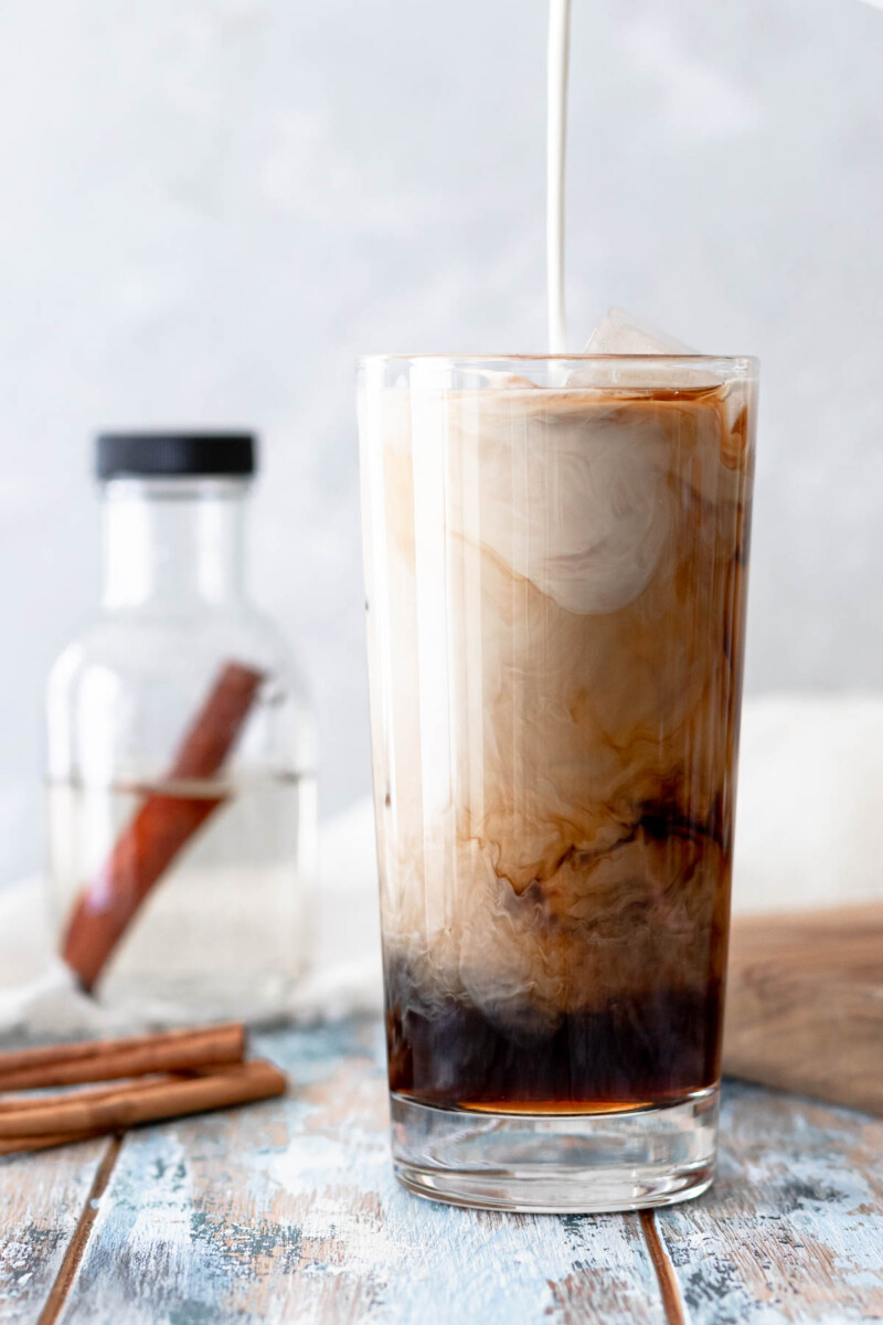 Milk pouring into a glass of cold brew coffee. You can see the swirls as the milk disperses in the coffee.