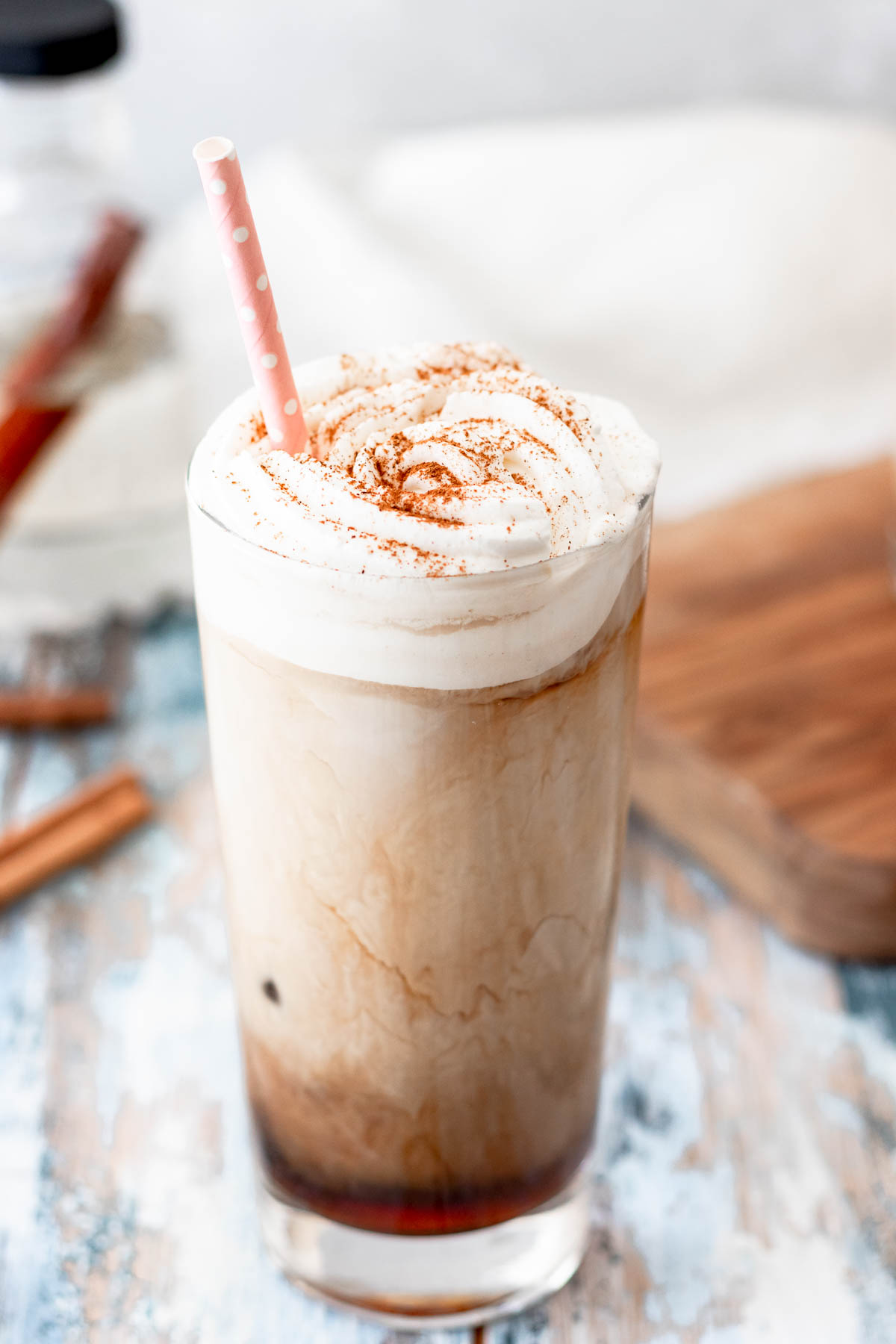 angled top view of a prepared glass of iced coffee with whipped cream topping and a dusting of cinnamon