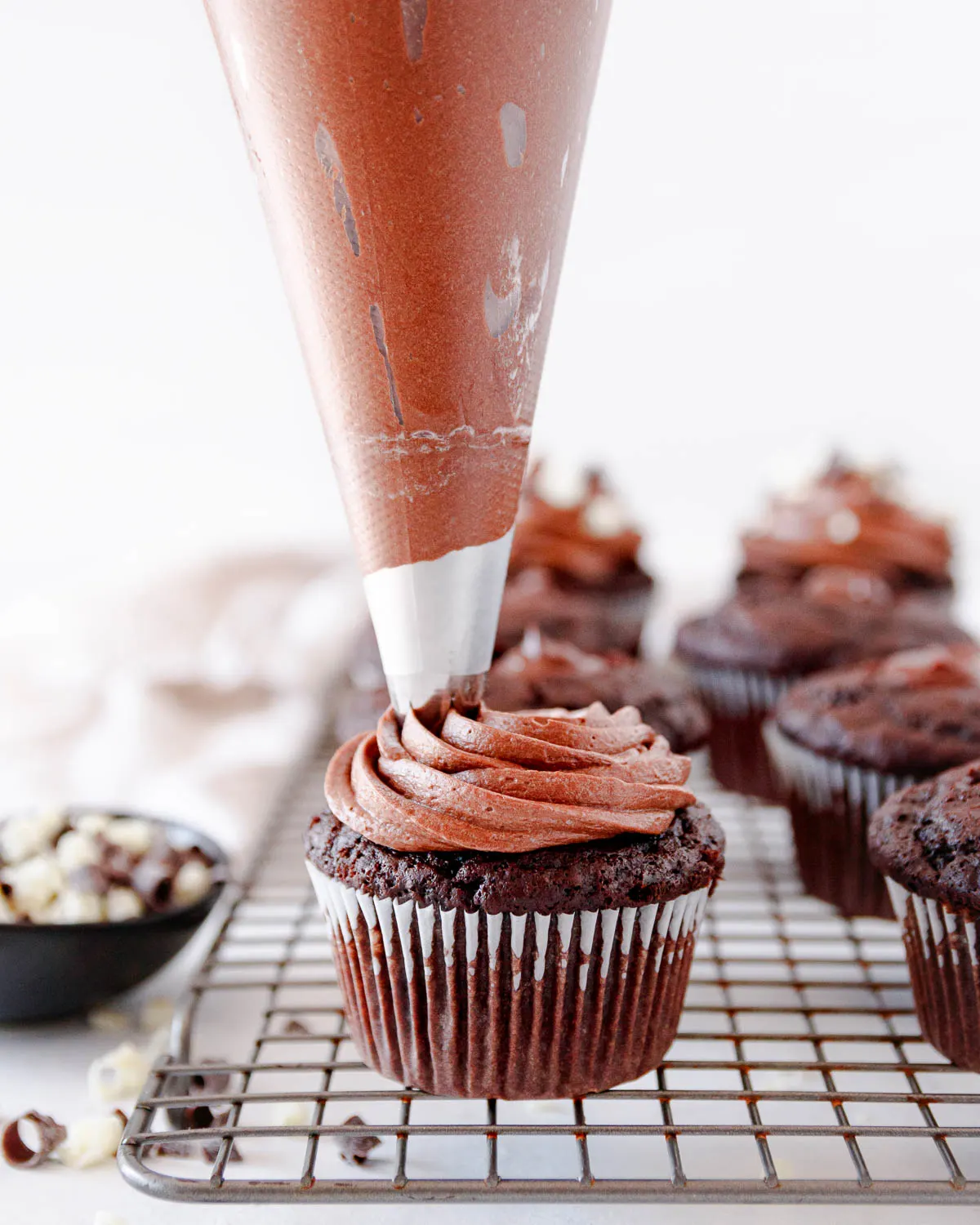 Piping bag swirling fudge frosting over a cupcake