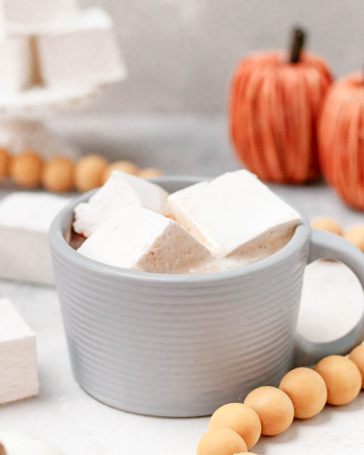 angled image of 3 pumpkin spice marshmallows floating in hot cocoa served in a pale grey mug