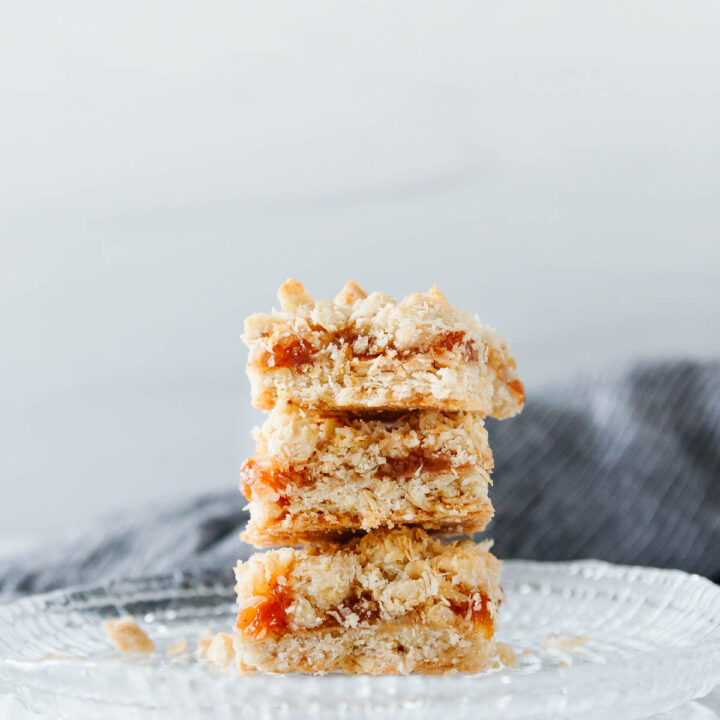 Three stacked coconut peach crumb bars on a cut glass plate with a dark grey napkin in the background.